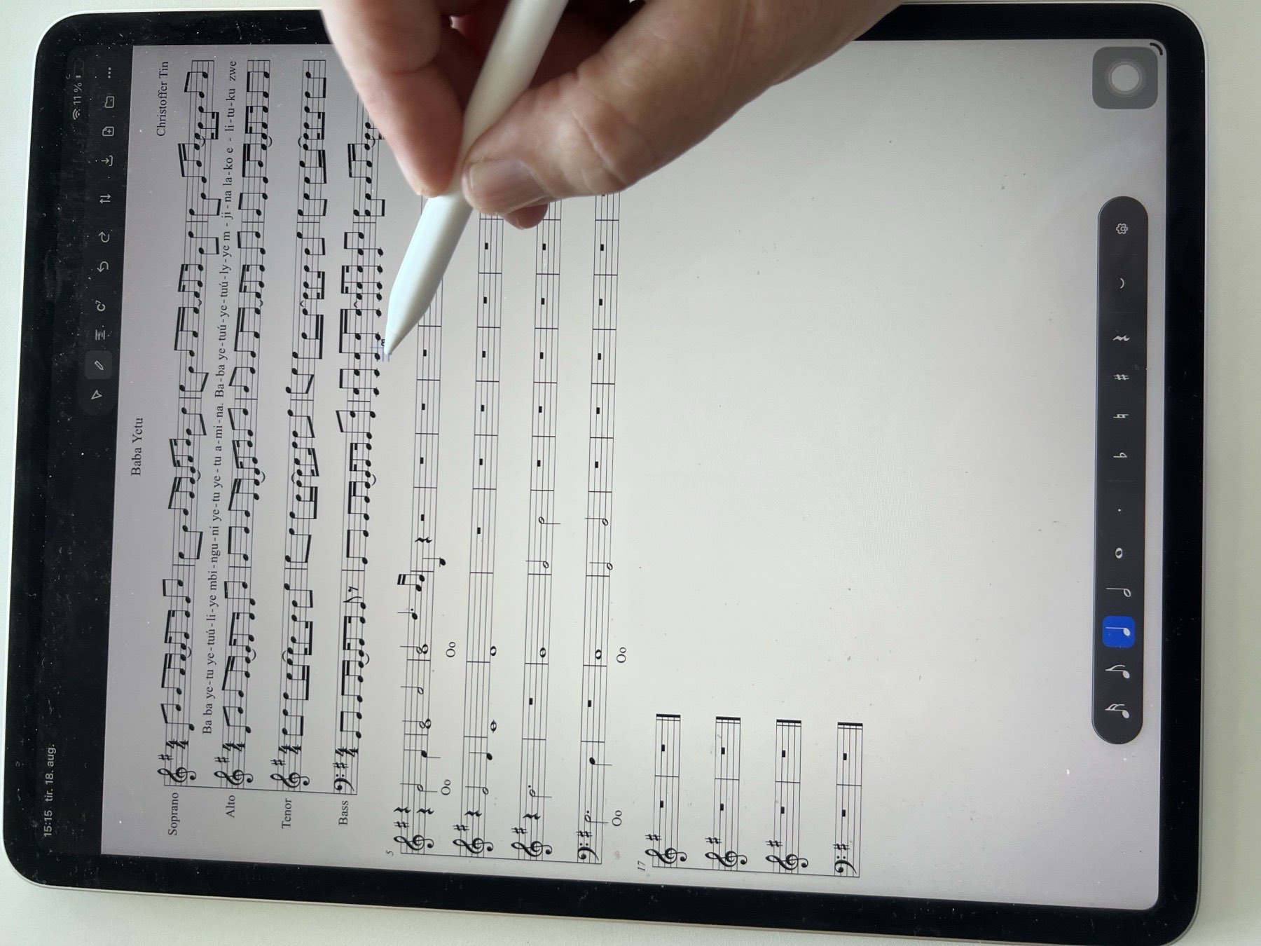 An iPad running Noteland with a four-part score open, a hand entering notes with the Apple Pencil
